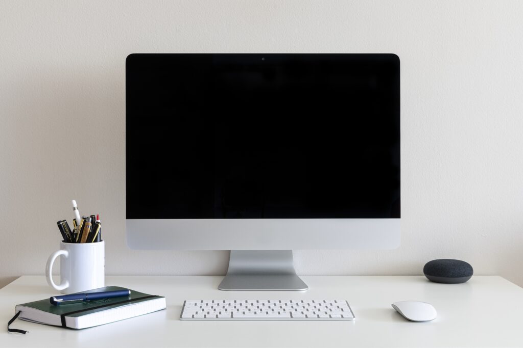 work desk with a computer, a cup with pens and pencils against a white wall